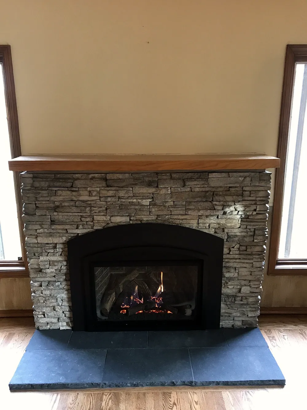 After: stacked stone fireplace face with an arched insert and new dark hearth