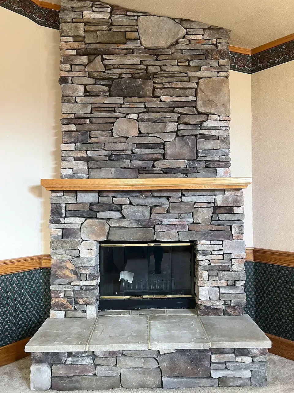 After: gray stacked stone to the ceiling with a natural wood mantel and stone hearth
