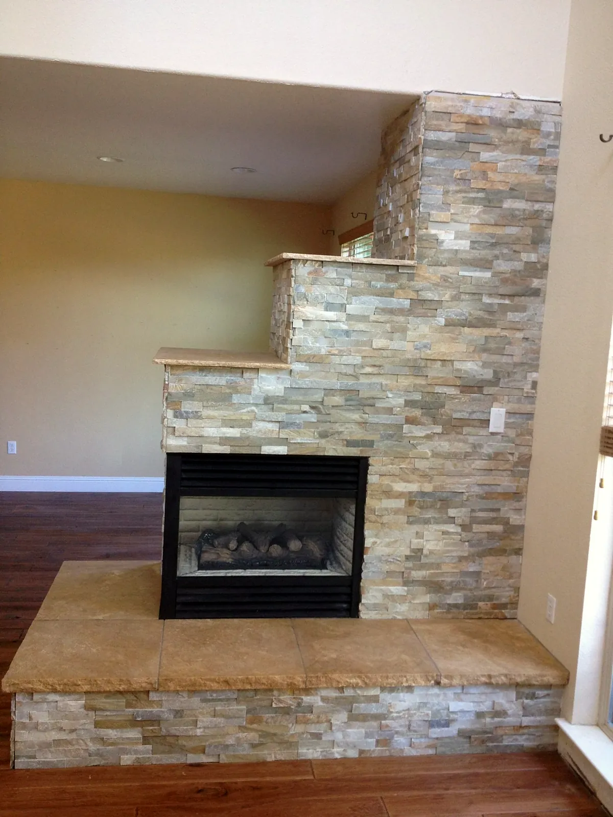 Front view of the same see-through corner fireplace with its long stone bench hearth