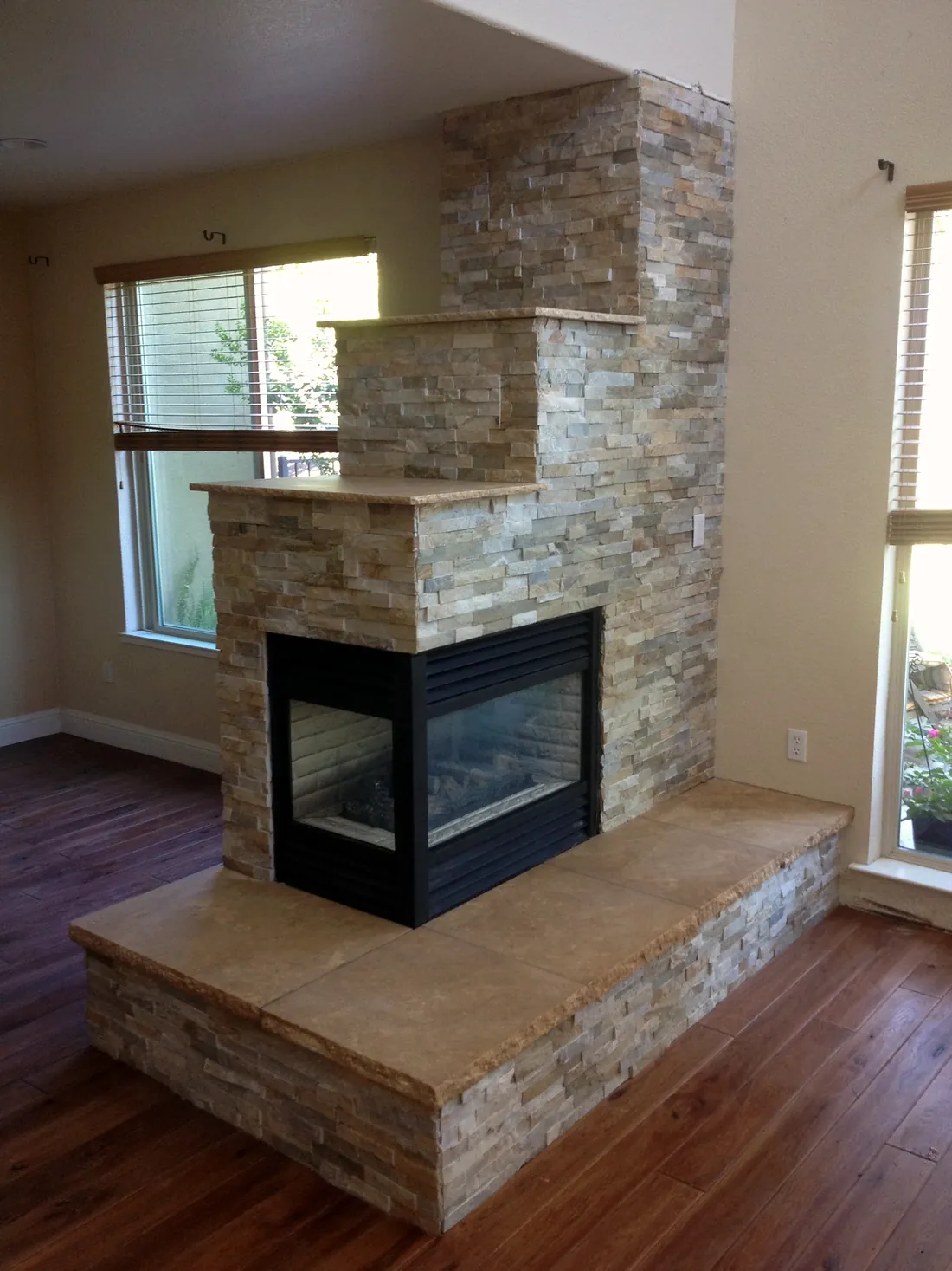 Stone-clad see-through corner fireplace with a long built-in stone bench hearth