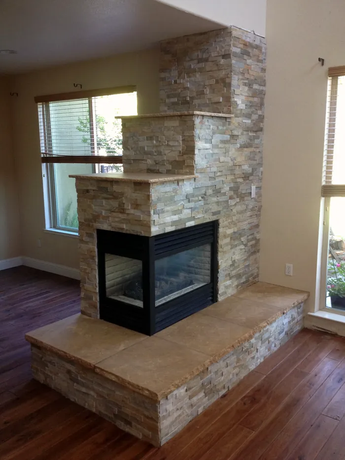 Stone-clad see-through corner fireplace with a long built-in stone bench hearth