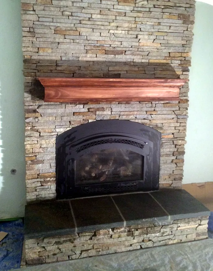 Stacked stone fireplace with an arched insert, stained wood mantel and wide stone hearth